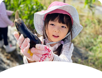 収穫したナスを持つ園児